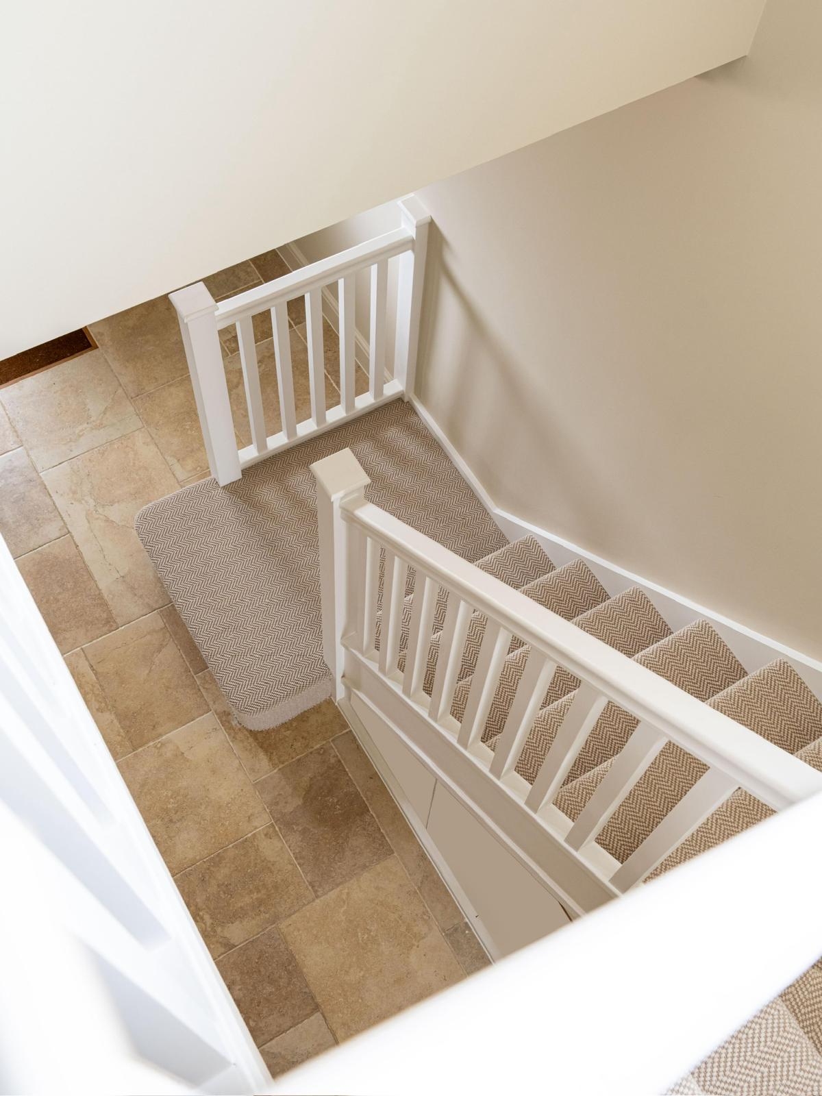 A bespoke staircase with a white painted balustrade, seen from the landing above